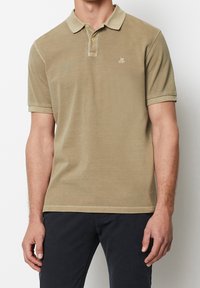 Beige polo tričko vyrobené z měkké tkaniny, s knoflíkovým límečkem, krátkými rukávy a malým vyšitým logem na hrudi.