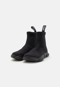 Botas de tobillo elásticas negras con un upper de tejido texturizado y una suela de goma acolchada. Presentan tiradores etiquetados como "CAMPER" en cada bota.