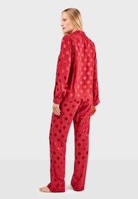 Conjunto de pijama de satén rojo que incluye una camisa con cuello y mangas largas, acompañada de pantalones con puntos. Textura suave, corte relajado.