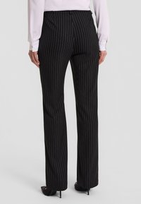 Czarne spodnie w paski z prostym krojem i gładką teksturą. Posiadają średniej wysokości talia oraz subtelne boczne kieszenie, zestawione z obcasami.