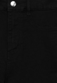 Jean en denim noir en gros plan montrant la poche avant, la boucle de ceinture et le bouton argenté avec gravure de la marque.