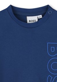 T-shirt blu navy con collo rotondo, caratterizzato da un tessuto testurizzato e una stampa del logo "BOSS" in blu audace sulla parte anteriore. Include un dettaglio con bottone a pressione.