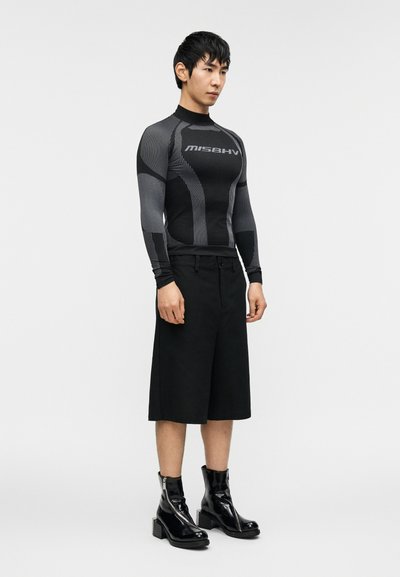 Μαύρο μακρυμάνικο τοπ συμπίεσης με υφασμένο μοτίβο και γκρι λεπτομέρειες, συνδυασμένο με μαύρο σορτς μέχρι το γόνατο και γυαλιστερά μαύρα μποτάκια στον αστράγαλο.