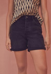 Shorts de mezclilla negra con dobladillos enrollados, con cintura alta y bolsillos frontales, combinados con una blusa estampada en tonos neutros.