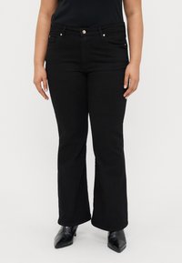 Jean évasé noir avec une taille mi-haute, comportant deux poches avant, des boutons dorés et un tissu lisse, légèrement texturé.