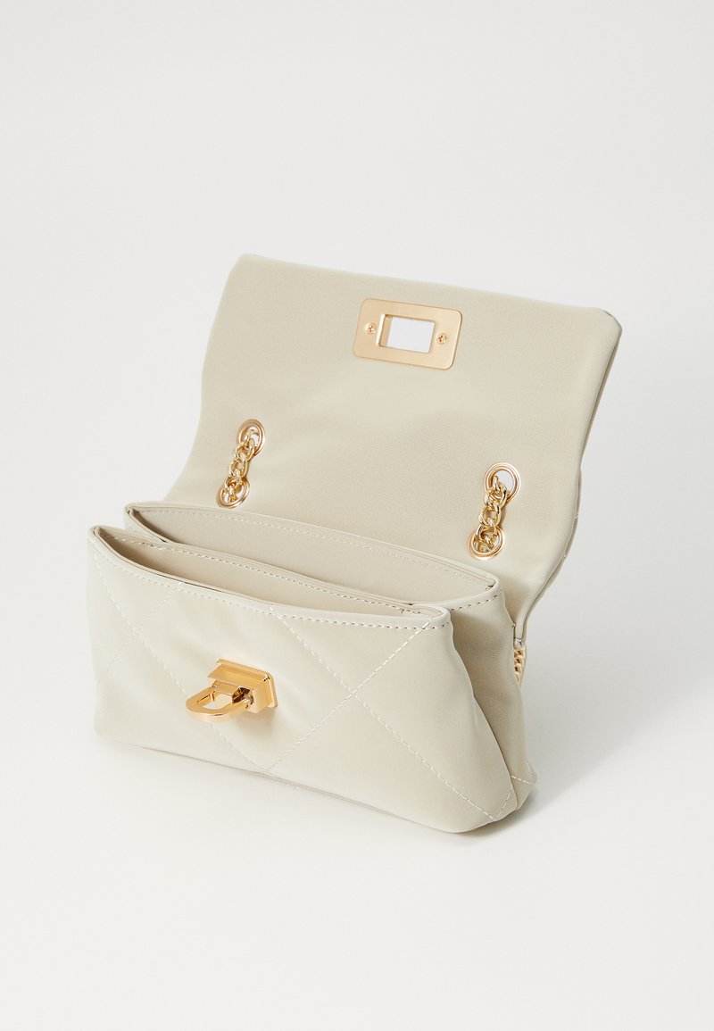 Sac à main beige matelassé avec quincaillerie dorée, doté d'une fermeture à rabat et de deux compartiments intérieurs. Texture lisse, design minimal.