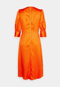 Robe en satin orange avec manches bouffantes, longueur mi-longue, motif à pois et fermeture éclair dorée au dos.