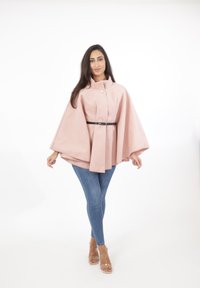 Ljusrosa kappa med hög krage, med en central knapp och ett svart bälte. Matchad med blå slim fit jeans och genomskinliga sandaler.