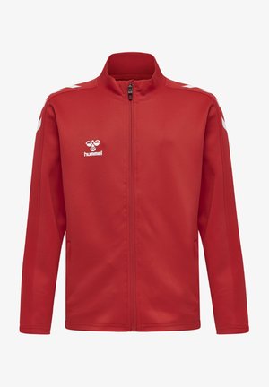Veste de sport rouge avec un col haut, fermeture éclair sur le devant et accents blancs sur les épaules. Arborant le logo Hummel sur la poitrine. Texture lisse.