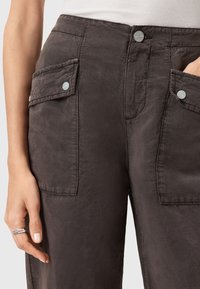 Pantaloni cargo grigi scuri con due tasche frontali con chiusura a scatto, tessuto testurizzato e vita alta. Dettagli con bottone frontale visibili.