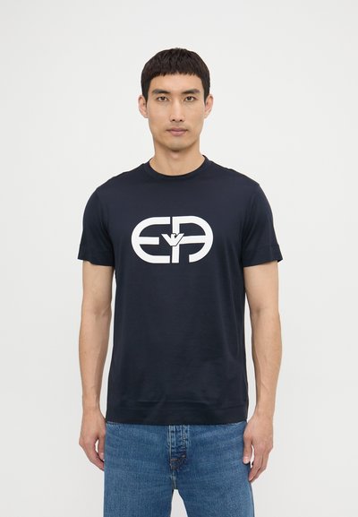 Granatowy bawełniany T-shirt z dużym białym logo z przodu. Okrągły dekolt, krótkie rękawy i luźny krój.