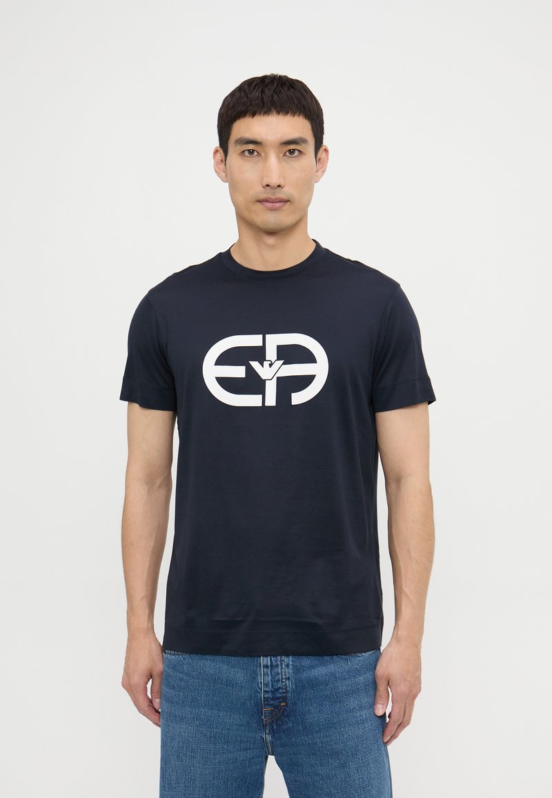 Tricou din bumbac bleumarin cu un design mare al logo-ului alb pe față. Decupaj rotund, mâneci scurte și o croială lejeră.