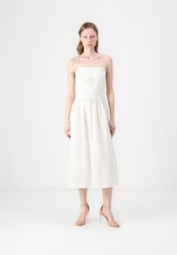Vestido blanco de lino con un corsé ajustado, escote cuadrado y tirantes ajustables; presenta un patrón de diamantes texturizado en la parte frontal.