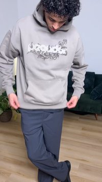 Hellgrauer Hoodie mit einem schwarzen Blumendesign, einer Fronttasche und einer Kapuze mit Kordelzug. Kombiniert mit dunkelgrauen Hosen.