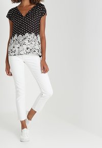 Černobílé top s puntíky a výstřihem do V, s krajkovým lemem ve květinovém vzoru, kombinované s bílými zkrácenými džíny a bílými teniskami. Hladká tkanina, volný střih.