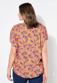 Korte mouw, vloeiende top in oranje met paarse bloemen- en paisleypatronen, met een gebogen zoom en ontspannen pasvorm.