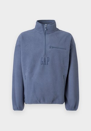Hele sinine fliisist pullover kõrge kraega, poollukuga ja rinnataskuga. Omab brodeeritud "GAP" logo ja elastseid varrukaid.