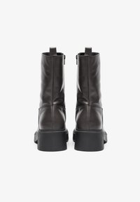 Bottines en cuir marron avec une semelle noire épaisse, dotées d'une fermeture éclair de chaque côté et d'une finition lisse. Le design est épuré et minimaliste.
