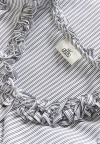 Black and white striped fabric with ruffled edges. A woven label with a logo is attached near the ruffle. Smooth texture.