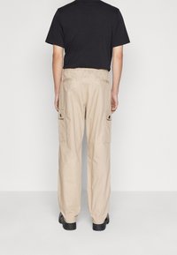 Beige cargobyxor med elastisk midja, sidofickor och avslappnad passform, tillsammans med en svart t-shirt. Slät tygtextur.