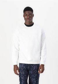 Vit crewneck sweatshirt i bomull med ribbad mudd och nederkant. Kombinerad med mörka mönstrade cargobyxor.