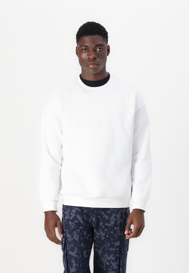 Vit crewneck sweatshirt i bomull med ribbad mudd och nederkant. Kombinerad med mörka mönstrade cargobyxor.