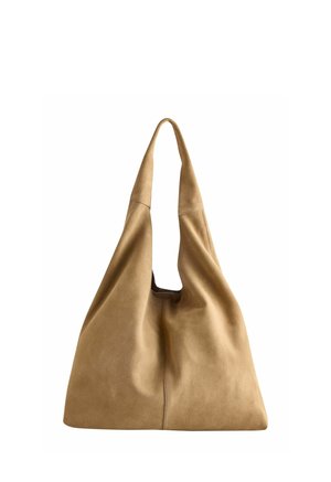 Zachte beige suède schoudertas met brede band en nonchalant, ongestructureerd ontwerp, afgebeeld tegen een witte achtergrond.