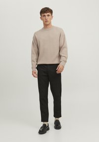 Maglione beige chiaro con collo rotondo, abbinato a pantaloni a quadri scuri e mocassini neri. Design semplice e texture non decorata.