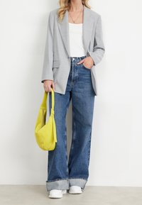 Veste oversize grise, débardeur blanc, jean bleu taille haute avec ourlet retroussé, et sac à bandoulière jaune vif. Baskets blanches.