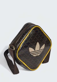 Geantă maro din piele cu un design rotunjit, având o suprafață cu model, margine galbenă și un logo proeminent de culoare deschisă cu trei dungi.