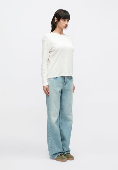 Μακρυμάνικο, απαλό λευκό ριγωτό πουκάμισο συνδυασμένο με φαρδιά ανοιχτό μπλε τζιν και γκρι-πράσινα αθλητικά παπούτσια. Καθημερινή εφαρμογή με χαλαρή σιλουέτα.