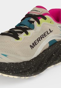 Ανοιχτό μπεζ αθλητικό παπούτσι Merrell με μαύρη σόλα με κηλίδες, μαύρα κορδόνια, τυρκουάζ λουράκι για κορδόνια, νέον κίτρινα στοιχεία και έντονη ροζ επένδυση στο εσωτερικό.