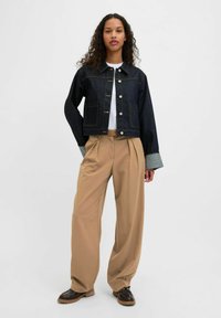 Donkerdenim cropped jack met zilveren knopen, twee voorzakken en contrasterende grijze manchetdetails, gecombineerd met beige wijde broek.