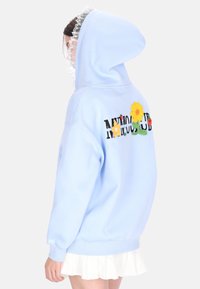 Hellblauer Hoodie mit großer Kapuze, verziert mit mehrfarbiger Blumenstickerei und dem Text „NIMBUS CLUB“ auf der Rückseite. Weicher Stoff und entspannter Schnitt.