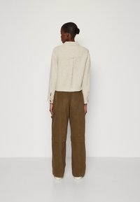 Lichtbeige cropped jas met kraag en rugplooien, gecombineerd met olijfgroene pantalon met wijde pijpen, voorzien van zakken en opgerolde manchetten.