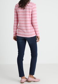 Rosa gestreiftes Langarmoberteil aus strukturiertem Strick, kombiniert mit dunkelblauen Skinny-Jeans und hellrosa Ballerinas, von hinten betrachtet.