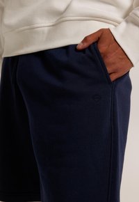 Marinblå bomullsshorts med en slät yta, med en sidoficka och en liten logotyp på nedre vänstra sidan.