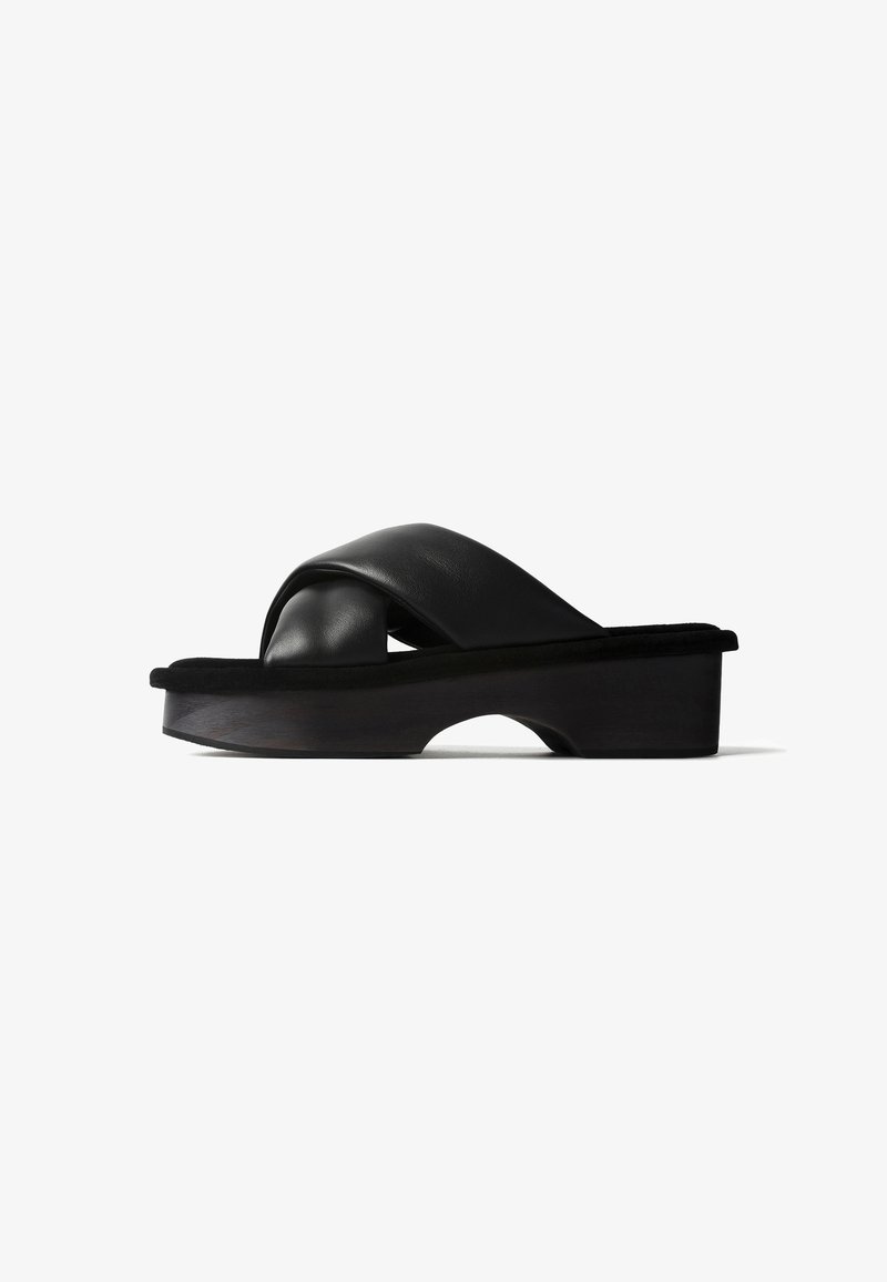 Sandale noire à enfiler avec des brides croisées en cuir matelassé et une semelle plateforme épaisse avec une petite découpe en arche.