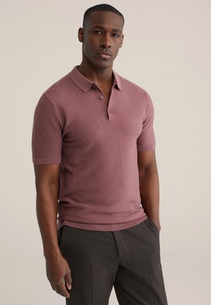 Lühikeste varrukatega polo pehme mauve toonis kampsunist, millel on kolme nupuga plastron ja soonikserv, kombineeritud tumeda halli paraja lõikega püksidega.