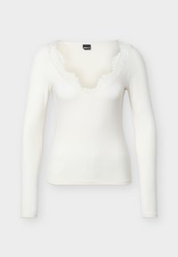 Valge pika varrukaga soonikkoes särk, millel on V-kujuline kaelus frustreeritud äärtega, eksponeeritud ühevärvilisel taustal.