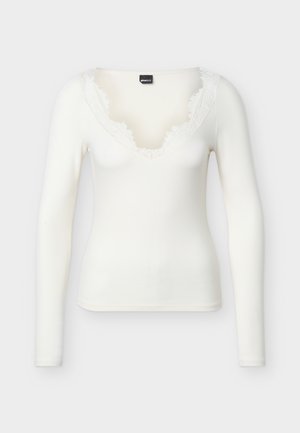 Biała, długorękawowa, prążkowana koszulka z dekoltem w szpic z postrzępionymi brzegami, prezentowana na jednolitym tle.