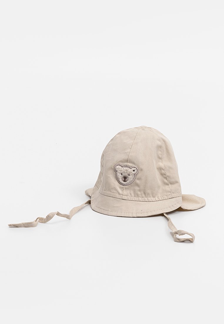 Beige Baumwoll-Bucket-Hut mit runder Krone, Kinnriemen und einer Bärengesicht-Stickerei auf der Vorderseite. Weiche Textur, breiter Rand zum Sonnenschutz.