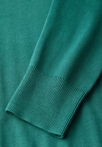 Teal knit sweater detail showing a ribbed cuff with a smooth texture, and a slightly loose fit. The fabric appears soft and flexible.