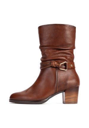 Botte en cuir marron mi-mollet avec tige souple, lanière nouée décorative, boucle dorée et talon bas en bois empilé.