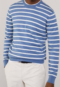 Modrý a bílý proužkovaný svetr z bavlněné směsi, s kulatým výstřihem a průramky s žebrovaným lemem, v kombinaci s kalhotami světle barvy.