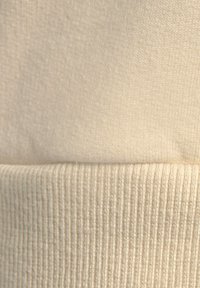 Tela de punto beige claro con superficie suave y textura acanalada en el dobladillo, mostrando puntadas uniformes y ligeras variaciones de tono.