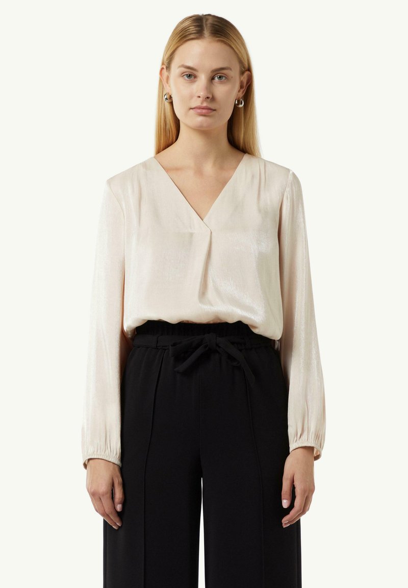 Bluzka w jasnoróżowym satynie z dekoltem w serek, z marszczonymi długimi rękawami, zestawiona z czarnymi spodniami o wysokim stanie z wiązanym paskiem.