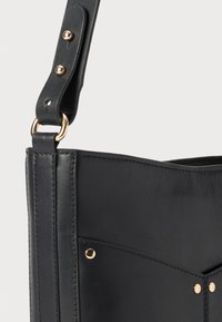 Sac à main en cuir noir avec un design structuré, présentant des accents en métal doré et des détails de coutures visibles. Sangle ajustable incluse.