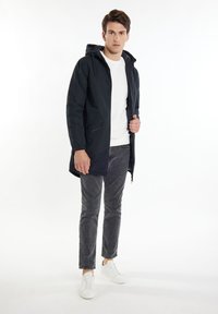 Mørkeblå polstret jakke med hætte, lynlås foran, elastiske ærmer, båret over en hvid t-shirt og grå bukser, parret med hvide sneakers.