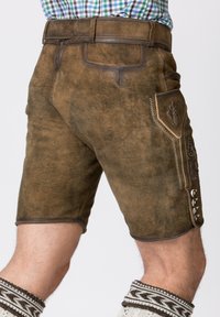Shorts in pelle marrone con finitura testurizzata, cuciture dettagliate, tasca laterale e accessori in metallo argentato. Abbinati a calze a ginocchio con motivo.